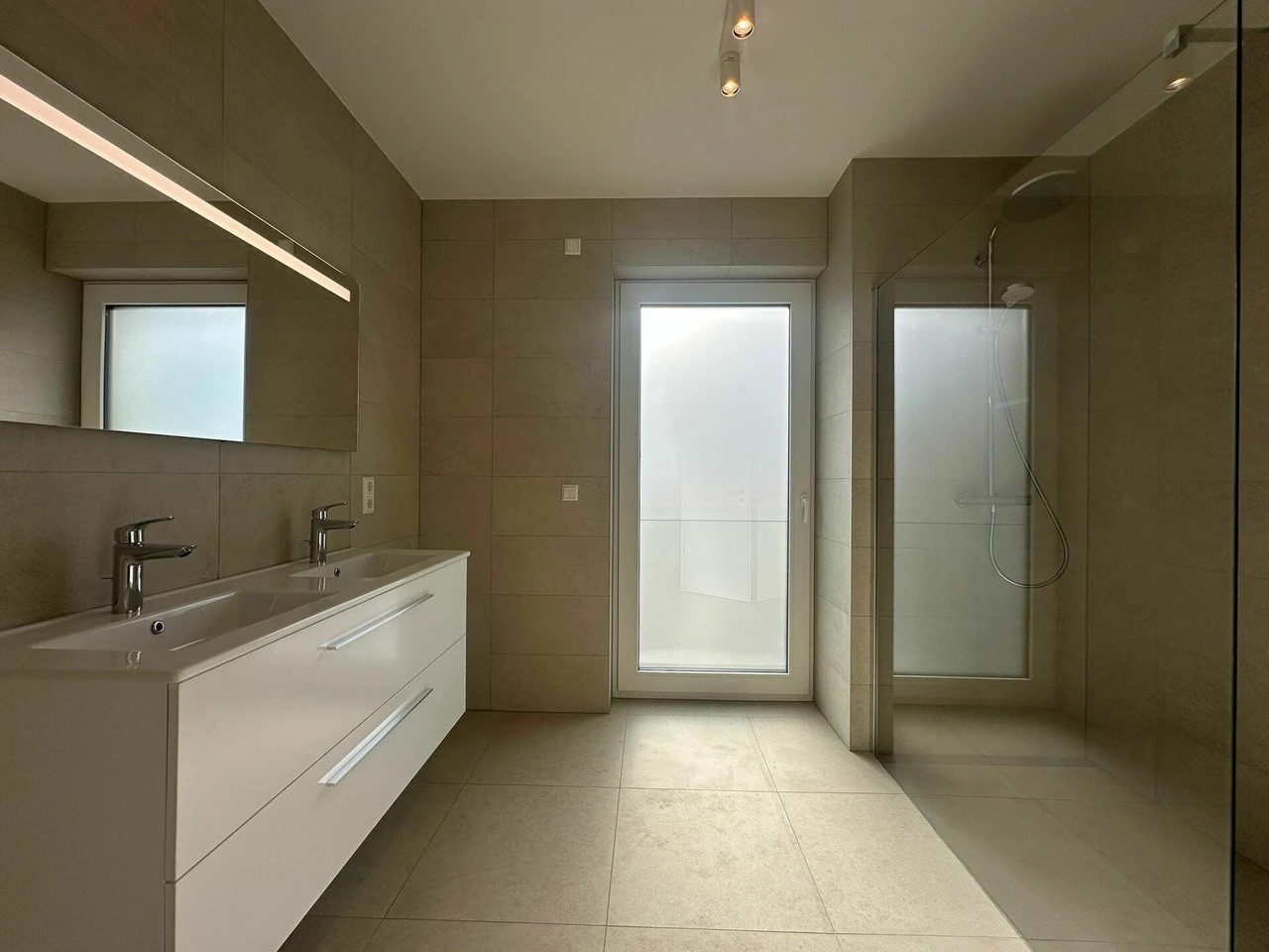 Salle de bain avec douche italienne, double vasque et carrelage beige